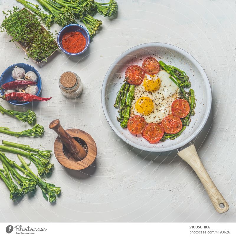 Fried eggs with tomatoes and broccoli in white frying pan on kitchen table with ingredients. Top view. Healthy breakfast fried eggs top view healthy cooking