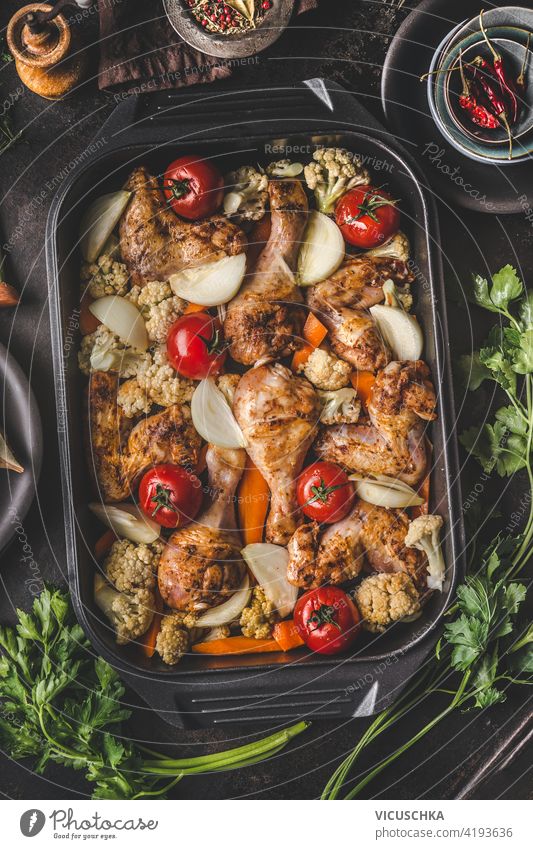 Tasty chicken drumsticks with vegetables  in cast iron pan on dark rustic background with fresh herbs. Healthy dieting food. Top  view. Chicken casserole tasty