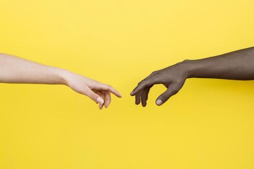 White hand and black hand about to touch on yellow background people friendship together clasped african international relationship skin unity copy space male