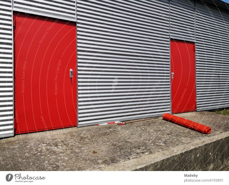 Red steel doors for fire protection in the shiny silver corrugated metal facade of an aircraft hangar in Oerlinghausen near Bielefeld in the Teutoburg Forest in East Westphalia-Lippe
