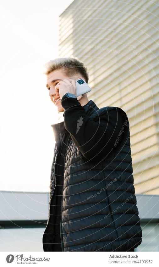 Positive young guy talking on smartphone and smiling near contemporary building man street smile phone call conversation communicate city cheerful male casual