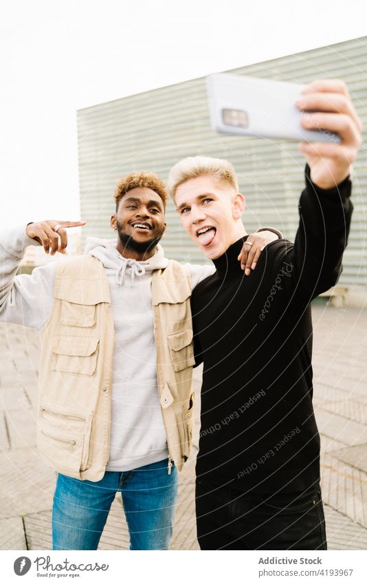 Positive young male friends making a self portrait with her smartphone on street men share smile happy together social media show tongue video mobile diverse