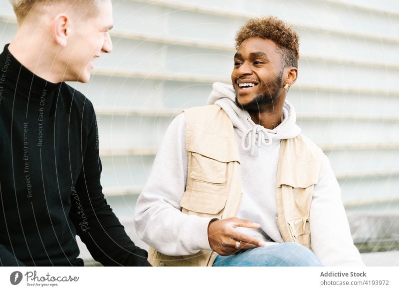 Positive young diverse guys standing on pavement in city district and smiling smile together friend street urban building exterior positive confident style