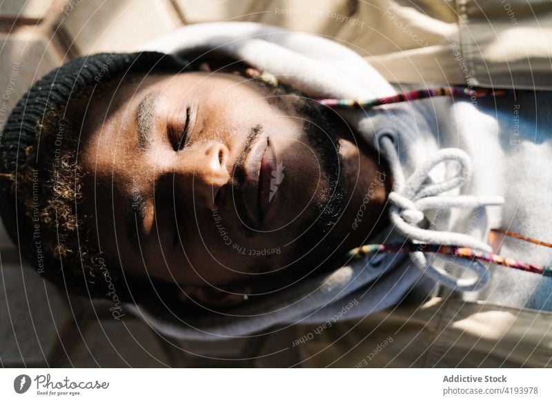 Young black guy sleeping on street in sunlight man eyes closed calm recreation city ground lying trendy harmony tranquil male young african american ethnic