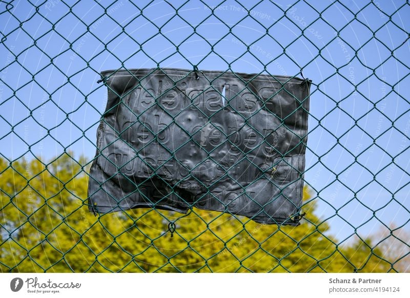 dented tin sign on chain link fence Wire netting fence Fence Tin Dented Signage Warning label DISREGARD Disrespect forbidden amateur football field trees warped