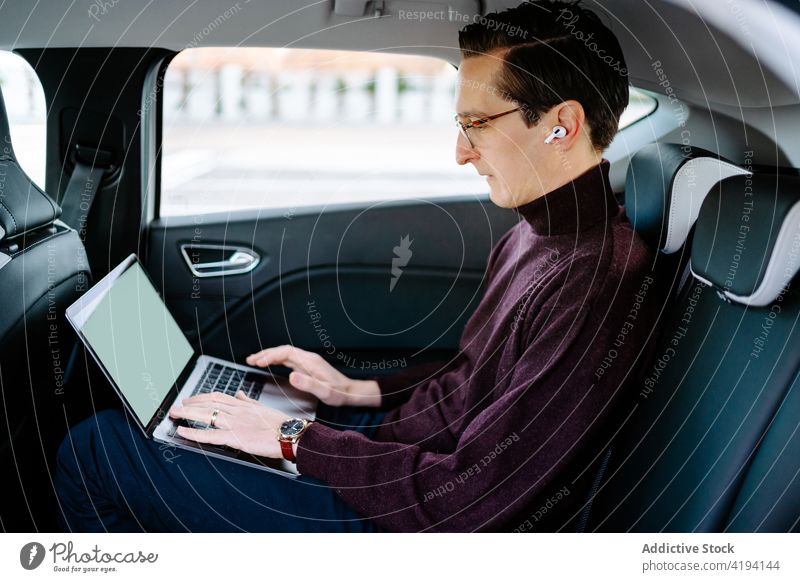 Focused businessman working on laptop in car browsing entrepreneur automobile typing luxury passenger male wireless earphones seat using professional internet