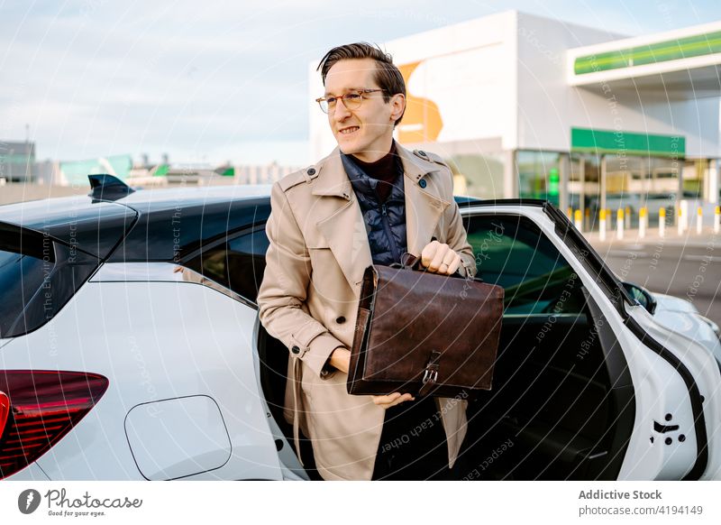 Smiling businessman with attache case getting out of car automobile smile entrepreneur transport handsome manager confident male coat style well dressed urban