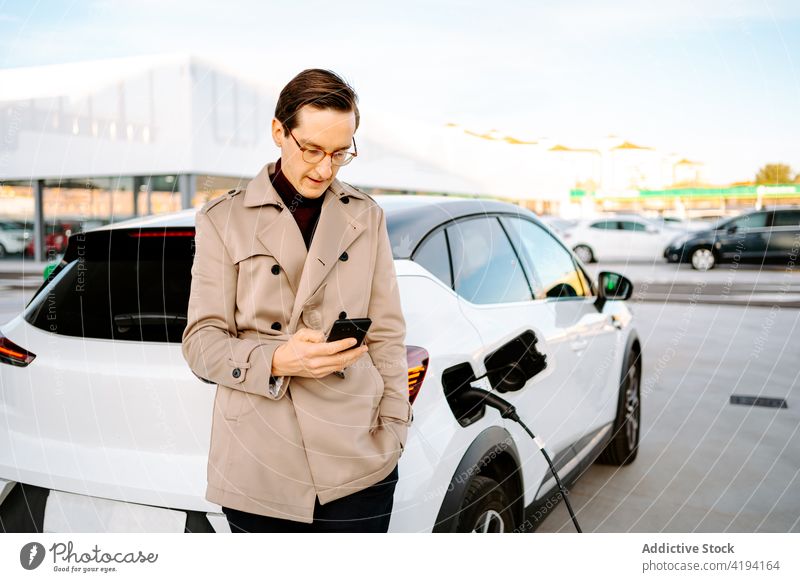 Businessman waiting for car refueling at gas station businessman fill petrol nozzle smartphone using male entrepreneur browsing online device lean gadget