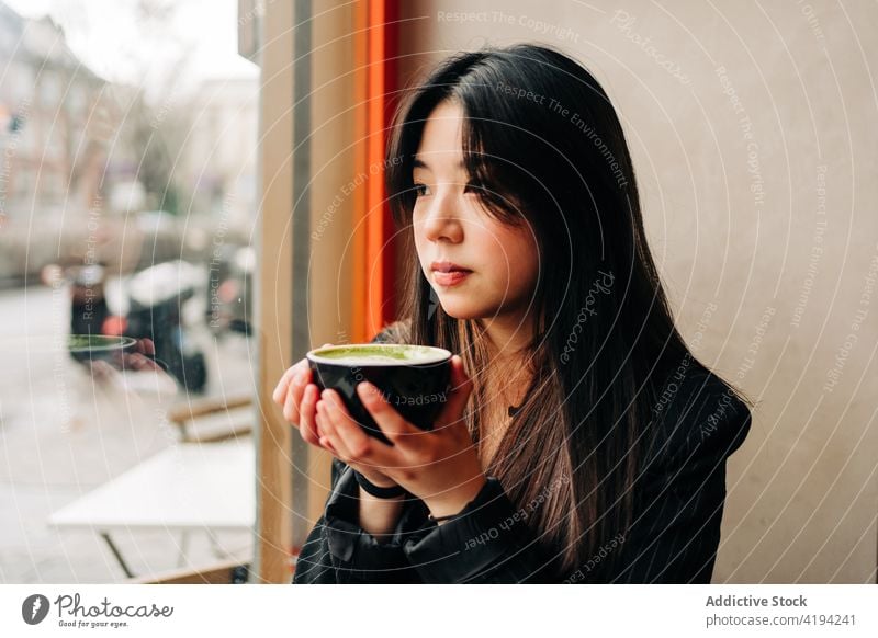 Long-haired brunette Asian woman having a coffee on a coffee shop while is looking a cellphone through the window asian people female chinese cafe cup person