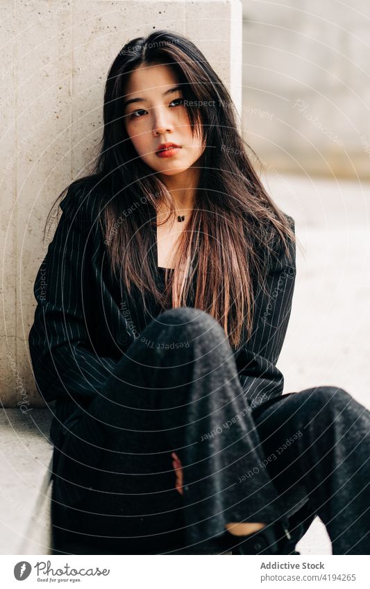 Long hair brunette asian woman sitting on some stairs and looking at camera japanese young female model chinese style attractive lady street modern stylish