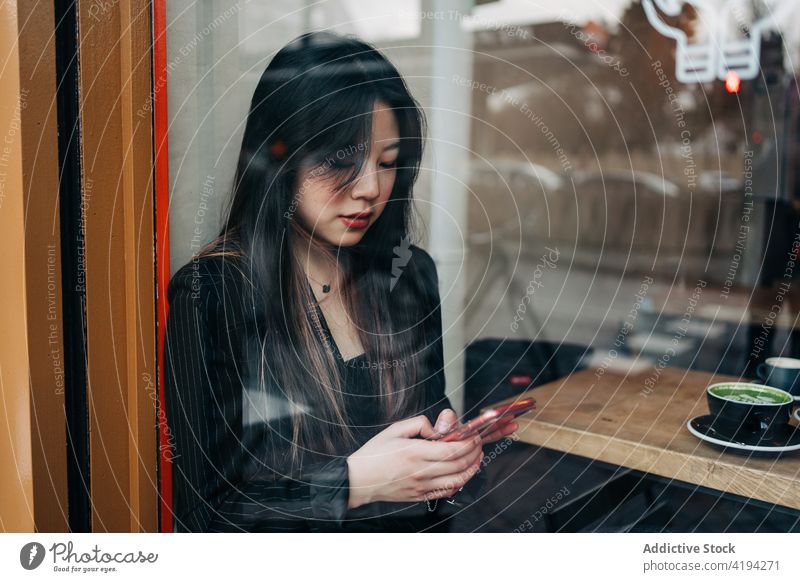 Long-haired brunette Asian woman having a coffee on a coffee shop while is looking a cellphone female asian chinese mobile cafe people cup person message