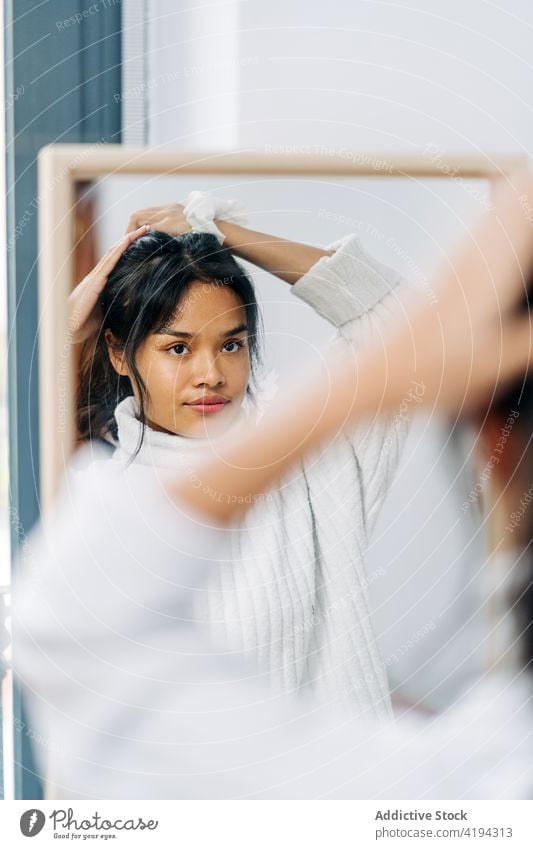 Long-haired brunette Asian woman dressed in a white sweater, looking in the mirror and combing her hair japanese asian young female model chinese style