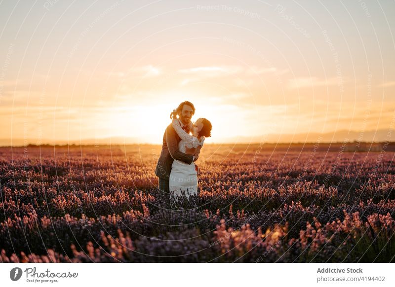 Happy newlywed couple hugging in lavender field at sunset lift bride groom wedding romantic dress suit nature white dress fancy gown tender marriage love