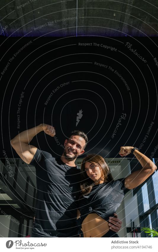 Positive strong couple showing biceps in gym bodybuilder muscle flex optimist hug power strength sport sportsman sportswoman bodybuilding workout muscular