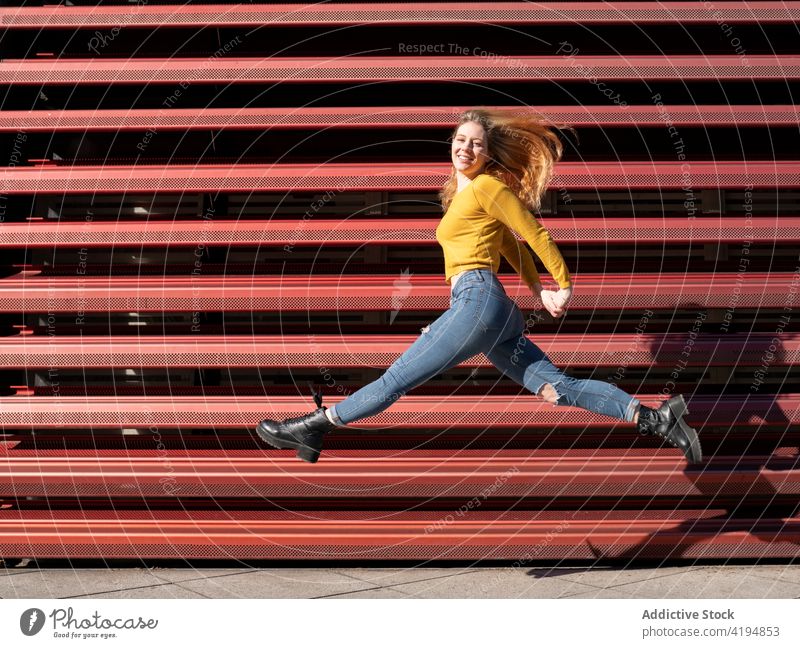 Joyful young woman jumping on street in sunlight smile energy joy cheerful active content optimist happy female casual millennial metal fence excited positive