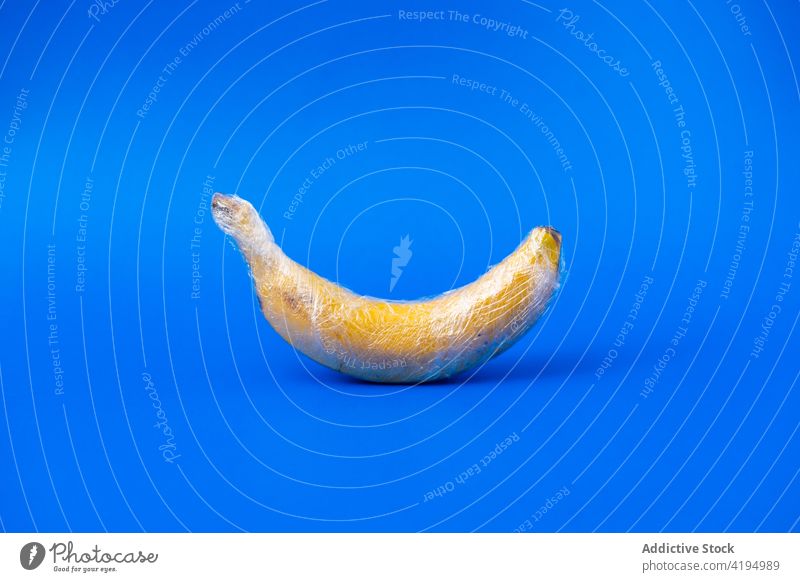 Fresh banana in food wrap on blue background agriculture industry overuse plastic concept fruit fresh ripe tasty whole vitamin nutrient natural product