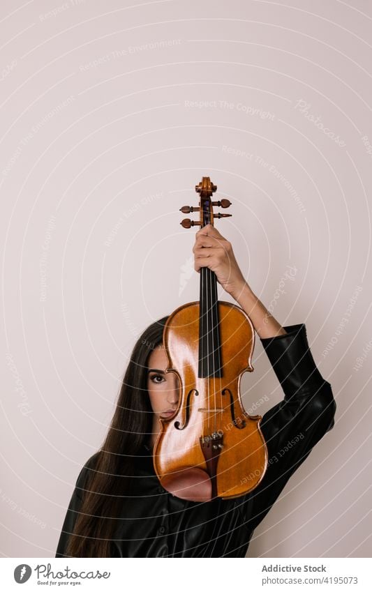 Musician hiding behind violin in studio woman player acoustic hobby music melody cover face art hide female artist professional musician talent skill instrument