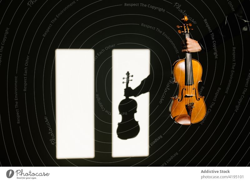 Crop faceless violinist demonstrating acoustic violin in dark room person musician instrument demonstrate string classic darkness window inspiration sound