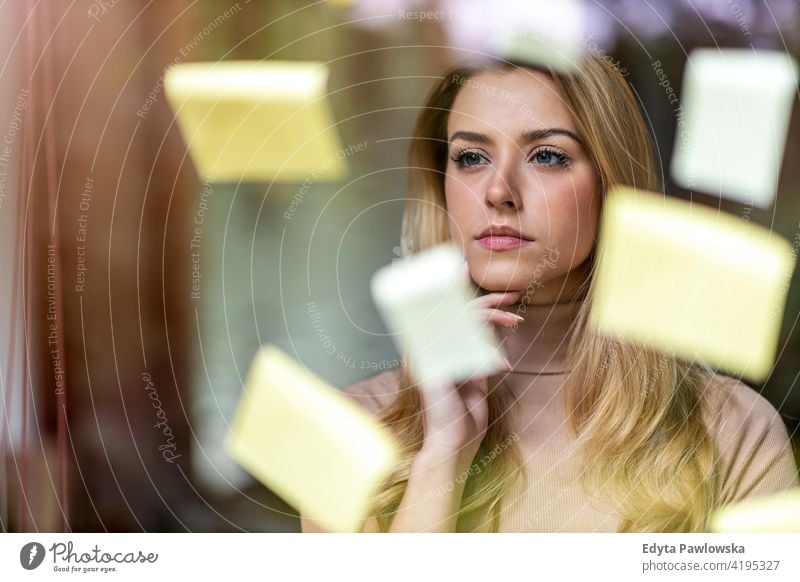 Young businesswoman brainstorming with notes on a glass wall in an office girl people Entrepreneur successful professional young adult female lifestyle indoors
