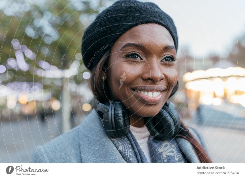 Smiling ethnic woman enjoying in city looking away headphones cheerful street song female black african american content device sound melody happy tune