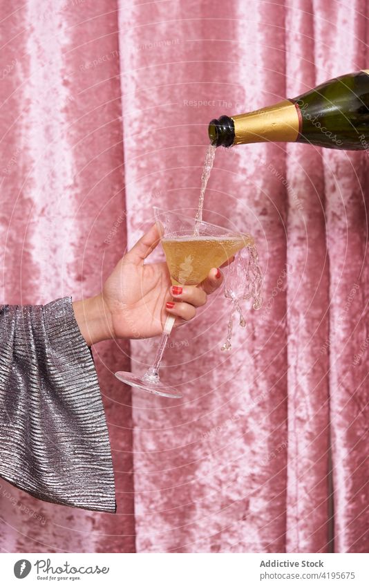 Crop woman with glass of champagne near velvet curtain bottle pour festive celebrate alcohol drink beverage alcoholic transparent flow occasion event shiny