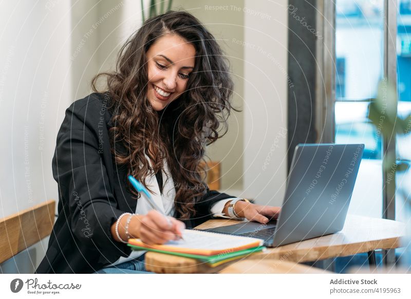 Female entrepreneur taking notes in notebook in cafe businesswoman take note work remote cheerful write laptop female planner table smile internet computer job