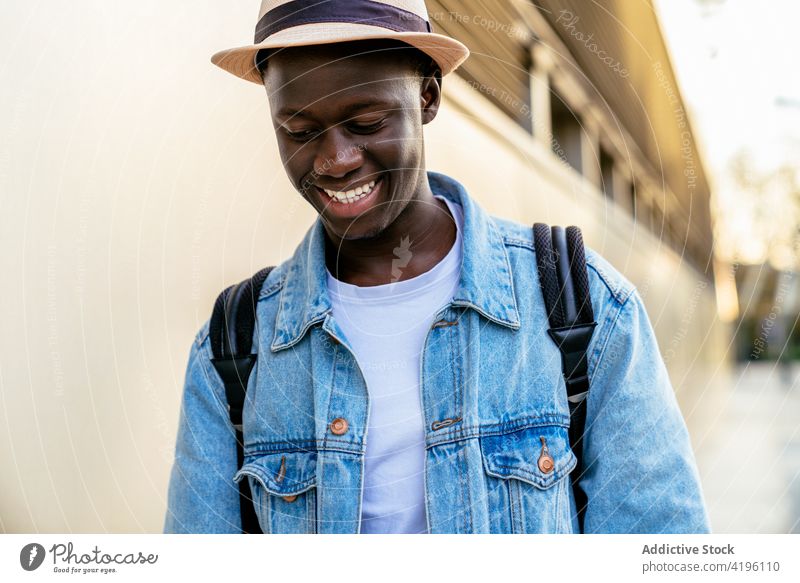 African-American man smiling near the wall cheerful sincere casual style friendly happy enjoy hand on hip denim jacket masculine bright modern cloth smile