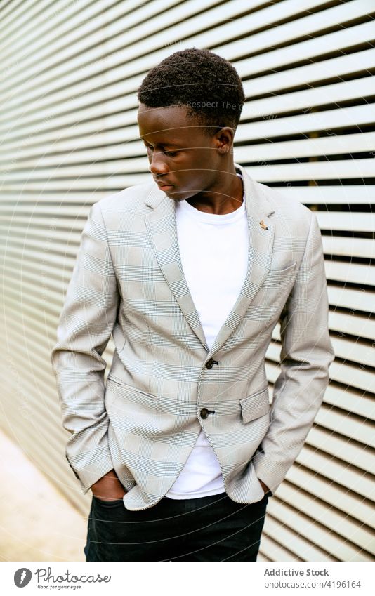 Stylish black man on urban pavement near ribbed wall stylish fashion masculine macho attentive model tiptoe town trendy apparel faded season style focus