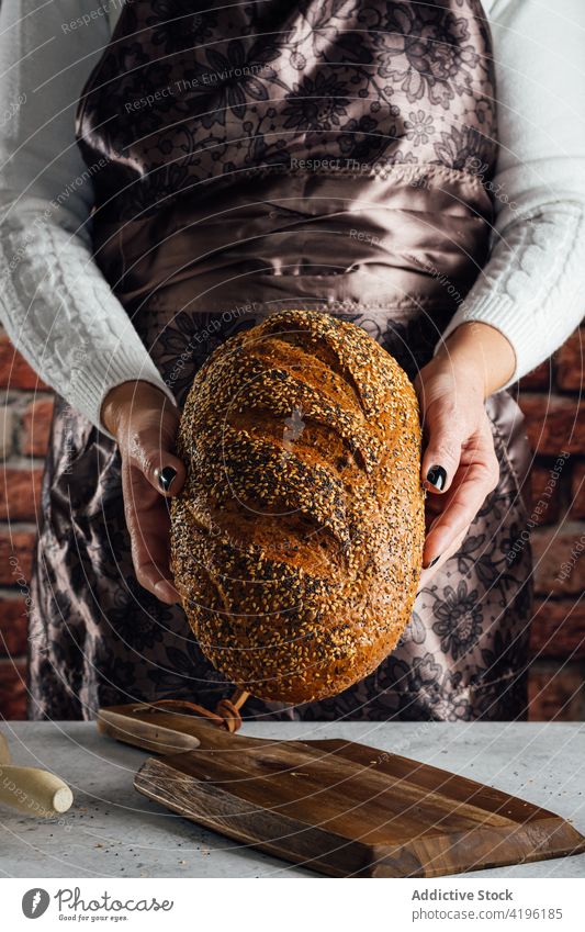 Crop artisan holding multigrain bread in bakery cut loaf nutrient cereal tasty bakehouse woman baked assorted rolling pin utensil knife sunflower seed fresh