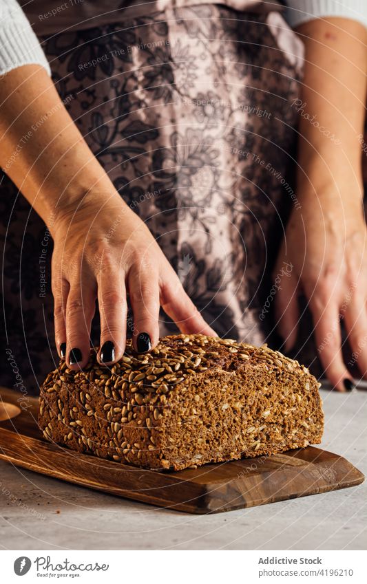 Crop artisan holding multigrain bread in bakery cut loaf nutrient cereal tasty bakehouse woman baked assorted rolling pin utensil knife sunflower seed fresh