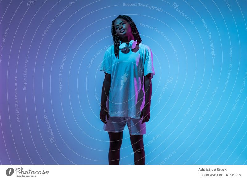 Black teen dancer in headphones in studio girl teenage light posture illuminate youngster neon cool glow generation urban bright modern confident style black