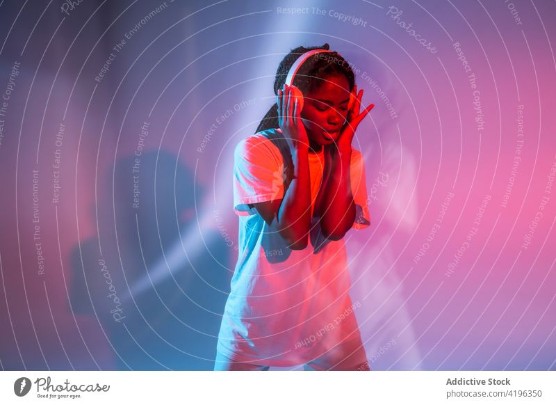 Expressive black teen girl listening to music in wireless headphones teenage enjoy expressive song neon playlist entertain young sound audio studio eyes closed