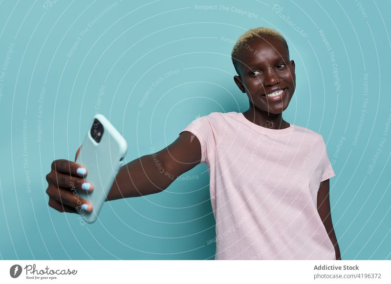 Cheerful black woman taking selfie in studio smartphone expressive African trendy feminine take photo moment studio shot toothy smile female mobile device