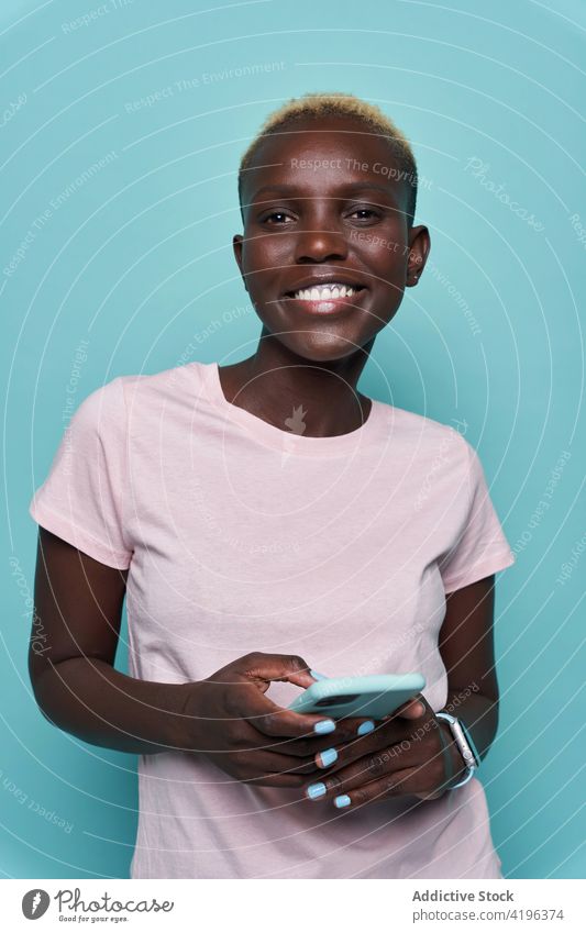 Cheerful black woman using mobile phone in studio smartphone expressive African trendy feminine studio shot toothy smile female device american style young