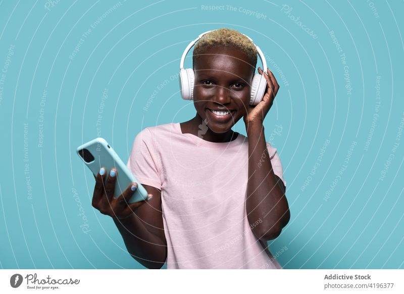 Excited black woman with headphones and smartphone music african charismatic expressive audio device song gadget female glad american mobile phone tune listen