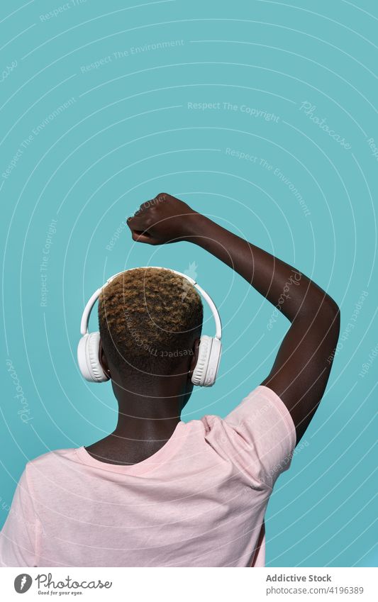 Black woman in headphones with raised arm arm raised studio shot listen music audio melody style gadget female device sound fist closed african american