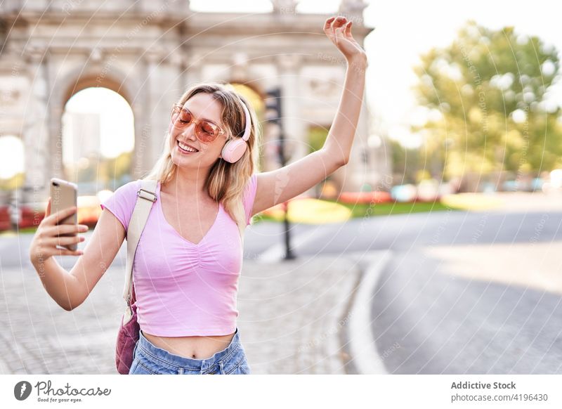Delighted teen woman taking selfie on smartphone teenage cheerful using music headphones listen sightseeing female device self portrait sunglasses optimist
