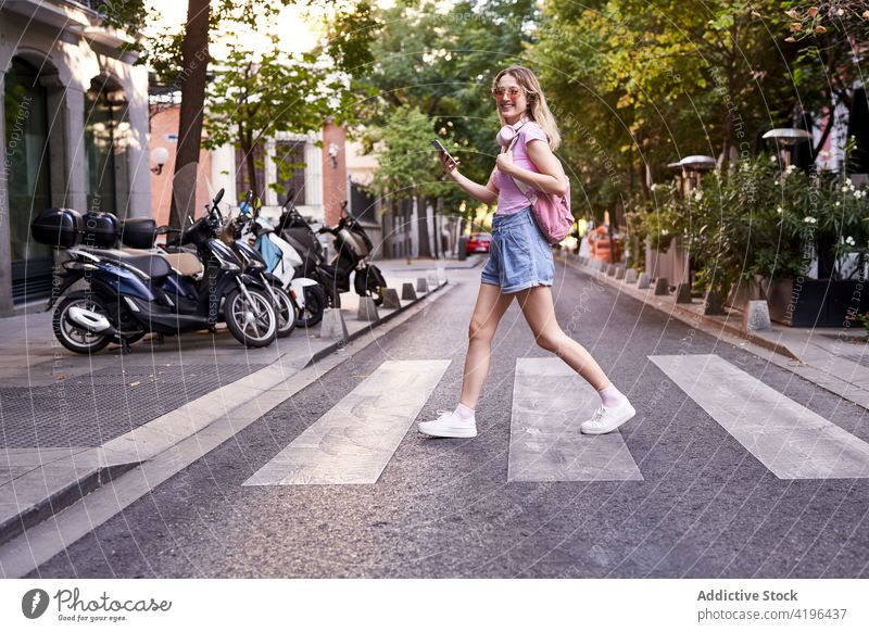 Positive teen tourist browsing smartphone while crossing road on zebra woman pedestrian check using route positive female vacation mobile online street