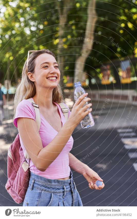 Smiling teen woman with bottle of water in park tourist holiday glad vacation journey female backpack teenage sunny optimist stand lifestyle drink delight city