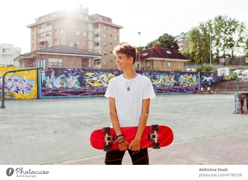 Handsome caucasian teenager with skateboard posing in the street back light basket boy city colorful court fun graffiti handsome happy horizontal leisure male