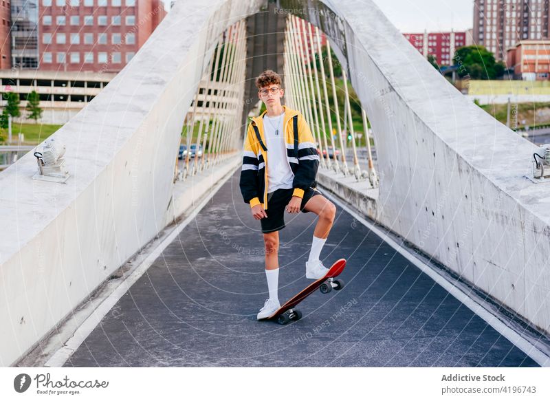 Caucasian teenager with skateboard standing on the bridge in the city autumn blonde boy caucasian colorful confident daylight horizontal leisure male man model