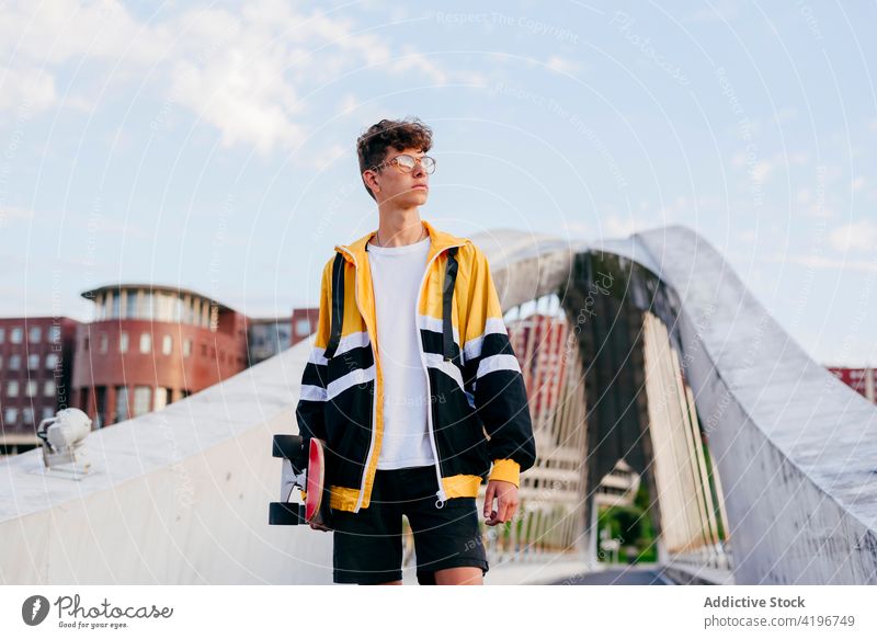 Caucasian teenager with skateboard standing on the bridge in the city autumn blonde boy caucasian colorful confident daylight leisure male man model one