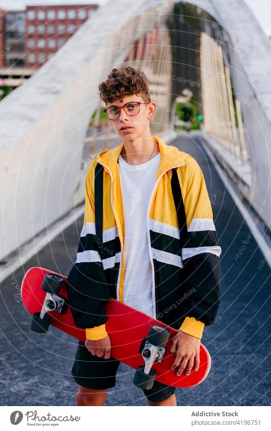 Caucasian teenager with skateboard standing on the bridge in the city blonde boy caucasian colorful confident leisure male man model one outdoors outfit posing