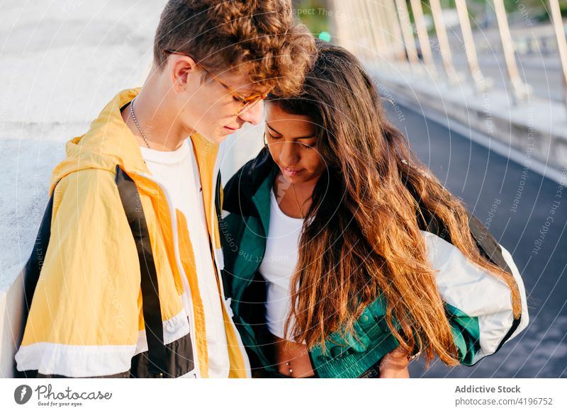Cropped couple of teenagers looking down in the street boy bridge caucasian city colorful daylight friends friendship girl hispanic horizontal jacket leisure