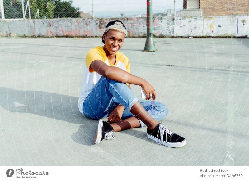 Handsome young black man sitting and laughing on the floor in the street attractive boy cap cheerful city colorful daylight ethnic handsome happy horizontal