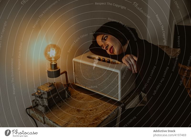 Tranquil woman looking at light bulb in vintage room dreamy retro daydream serene illuminate female radio set lean old fashioned pensive dark home lady style
