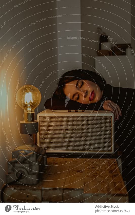 Tranquil woman with closed eyes and light bulb in vintage room dreamy retro daydream serene illuminate female radio set lean old fashioned pensive dark home