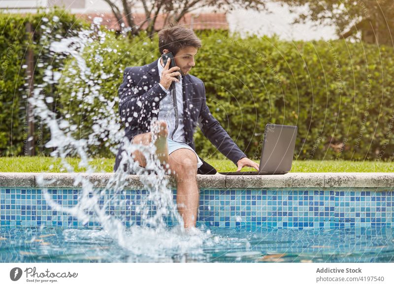 Businessman dressed in a suit sitting on the edge of the pool with a laptop work person businessman swimming computer phone talking speaking internet people