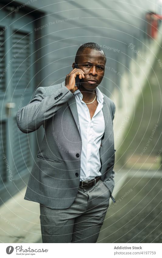 Serious black male boss speaking on smartphone in town african american black serious suit masculine hand in pocket man using gadget device phone call cellphone