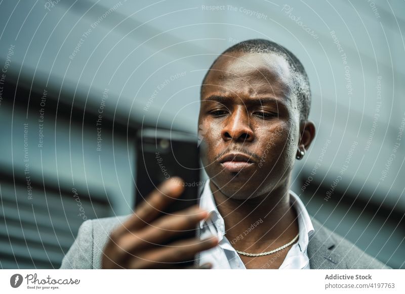 Serious black male boss browsing a cellphone in town smartphone african american black serious suit masculine man using texting gadget device communicate city